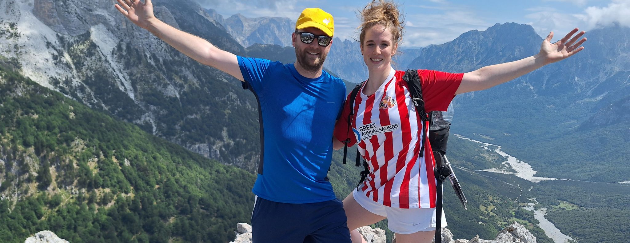 Woman and man hiking in the Albanian Alps, holding out their arms in celebration of their hike and smiling.