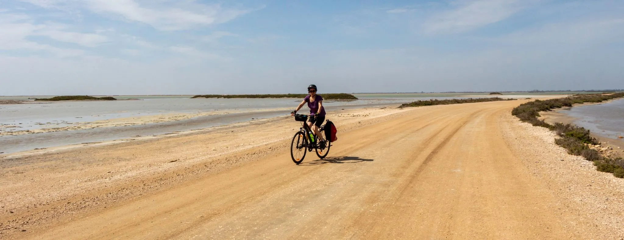 Young woman on a bike tour in the famous marshes of Camargue on a sunny day. She is riding on an earth path typical of this wetland. Arles, Salin de Giraud, Provence, France.